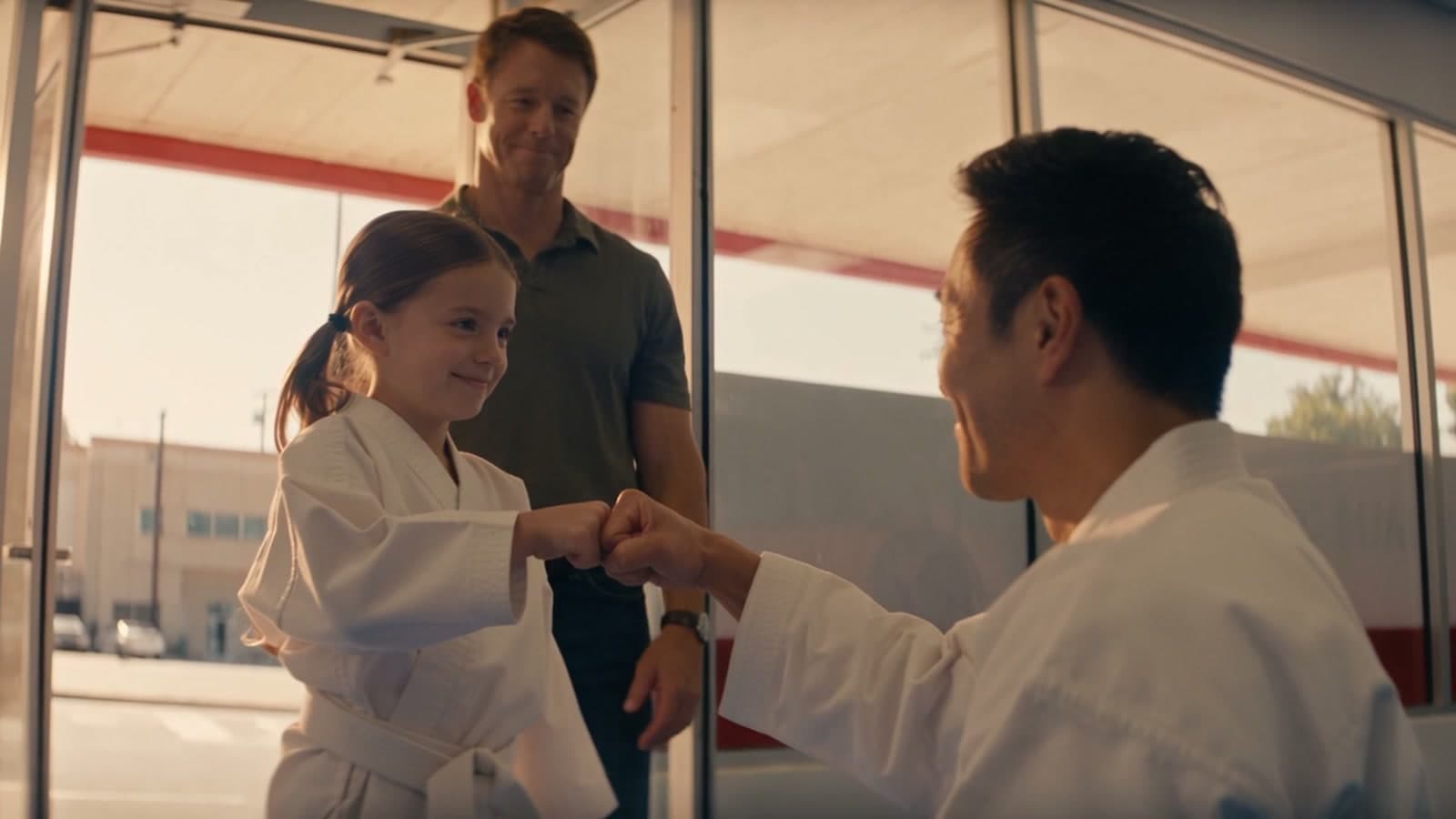 A girl in a white gi fist-bumping her instructor, with a parent standing behind them